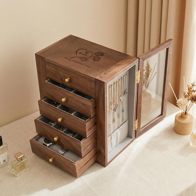 May include: A wooden jewellery box with multiple drawers and a glass-door compartment. The box is a warm brown colour with gold-coloured knobs and a decorative engraving on the top. The drawers are open, revealing jewellery and watches.
