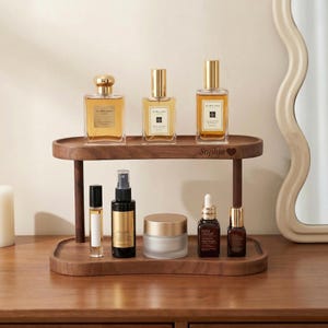 Peut inclure: Un pr&eacute;sentoir de vanit&eacute; en bois &agrave; deux niveaux avec plusieurs flacons de parfum et produits de soin de la peau. L'&eacute;tag&egrave;re sup&eacute;rieure contient trois flacons de parfum avec des bouchons dor&eacute;s. L'&eacute;tag&egrave;re inf&eacute;rieure contient un roll-on, un vaporisateur, un pot et deux petits flacons. Le plateau est grav&eacute; du nom "Sophia".