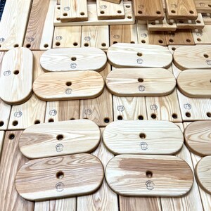 Puede incluir: Una colecci&oacute;n de tablas de cortar ovaladas de madera con un agujero en el centro. Las tablas son de madera clara con un patr&oacute;n de veta natural. Cada tabla tiene un logotipo circular quemado en la superficie.