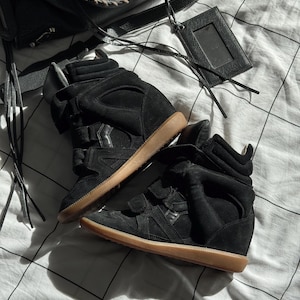 May include: A pair of black high-top wedge sneakers featuring suede and leather panels, hook-and-loop straps across the midfoot, padded collars, and gum rubber outsoles. The sneakers have a concealed wedge heel design and a high-cut silhouette.