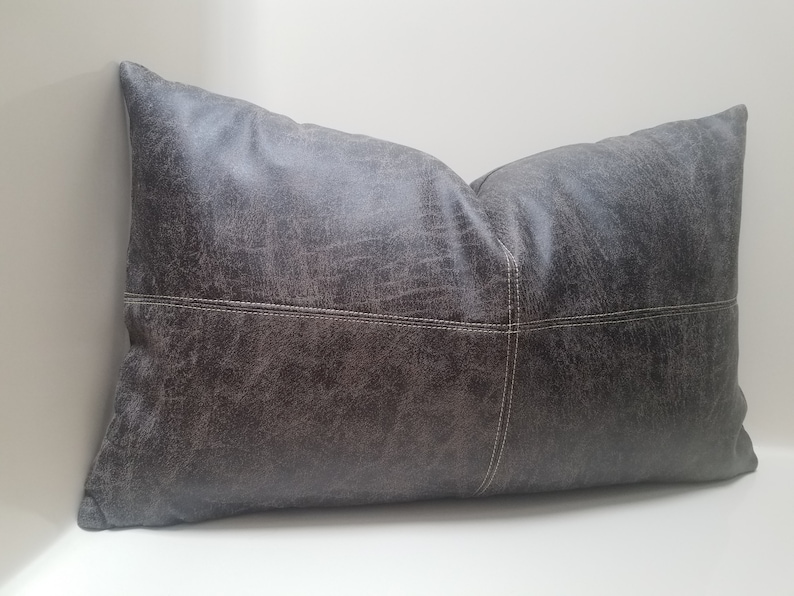 May include: A gray leather pillow with white stitching. The pillow has a distressed look and is rectangular in shape.