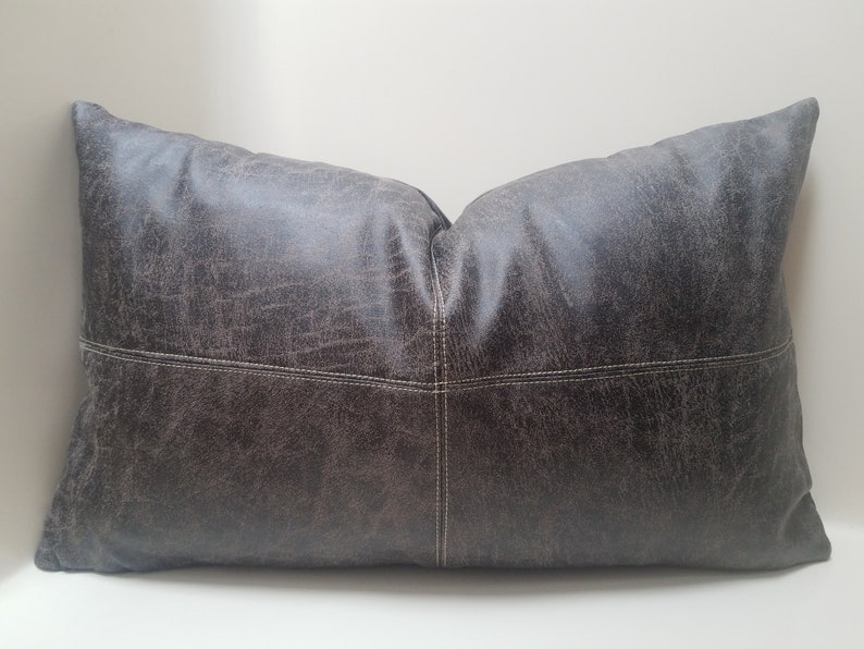 May include: A large, rectangular pillow with a dark gray, distressed leather-like fabric. The pillow has white stitching around the edges and a subtle diamond pattern.