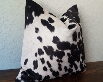 May include: Black and white cowhide patterned throw pillow. The pillow is made of a soft, comfortable fabric and has a subtle sheen.