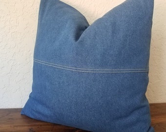 May include: A blue denim pillow with a white seam down the center.