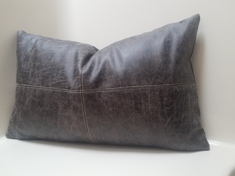 May include: A dark gray rectangular pillow with a textured faux leather cover. The pillow has white stitching along the seams.