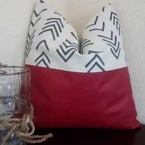 May include: A decorative pillow with a white fabric top featuring a black geometric pattern and a solid red bottom.