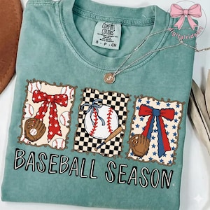 May include: A teal Comfort Colors t-shirt with a baseball theme. The shirt features three framed baseball designs with a baseball, glove, and bow. The words "BASEBALL SEASON" are printed in black script.