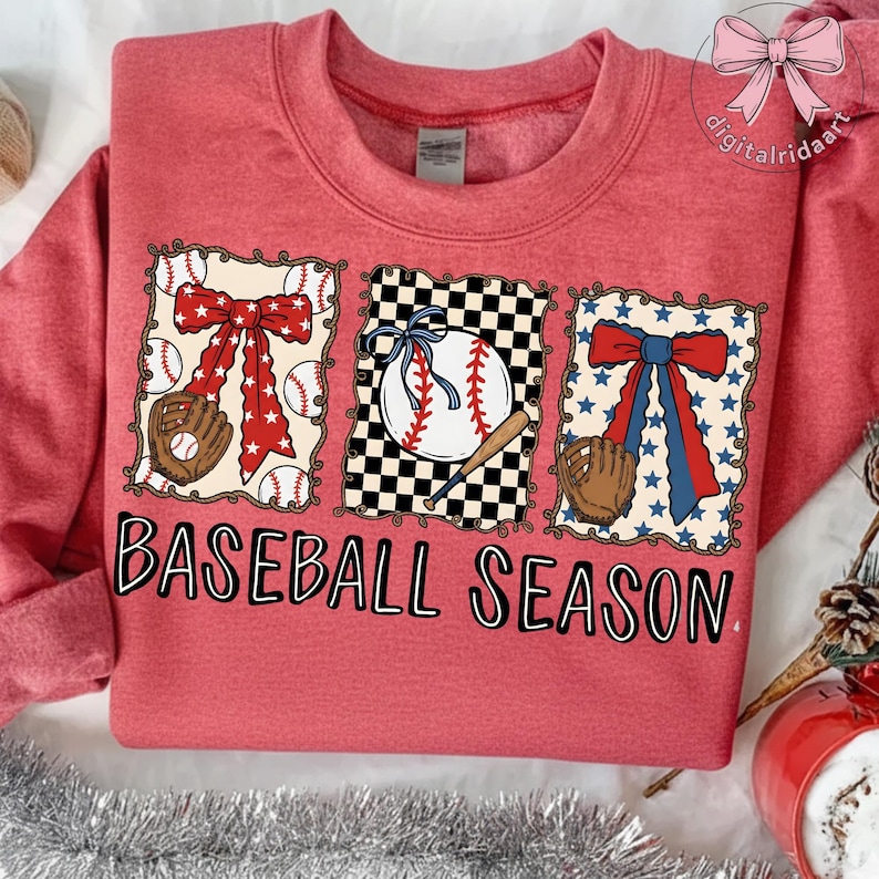 May include: Red sweatshirt with a baseball-themed design. The design includes a baseball, glove, and bow, with the words "BASEBALL SEASON" in black block letters.