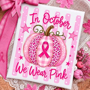 Op de afbeelding: Een rechthoekig bord met een roze en wit gestreepte achtergrond met de tekst In October We Wear Pink. Een centrale pompoenillustratie toont een roze luipaardprint en een roze vichy-patroon, geaccentueerd door een roze bewustzijnslint.