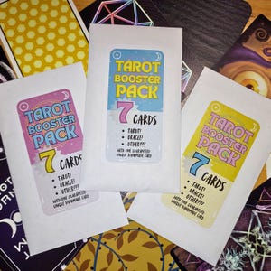 May include: Three white Tarot Booster Pack card packs with colorful labels. Each pack has the text "Tarot Booster Pack" and "7 Cards". The labels include the words "Tarot!", "Oracle!", and "Other???".