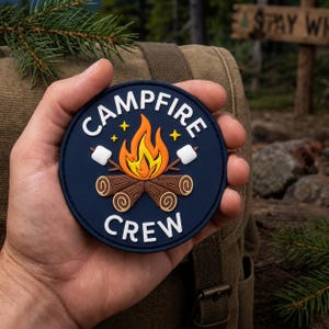 May include: A circular navy blue patch featuring a graphic of a campfire with orange and yellow flames, brown logs, and two white marshmallows on sticks. The text "CAMPFIRE" is arched above the fire, and "CREW" is printed below in white.