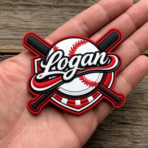 Puede incluir: Un parche circular de goma con una pelota de béisbol blanca con costuras rojas, cruzada por dos bates de béisbol negros. El nombre Logan está escrito en letra cursiva blanca en el centro. Incluye bordes rojos y negros y una pequeña estrella roja.