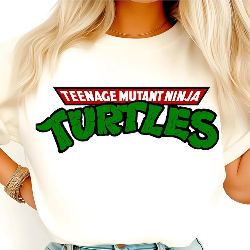 Pode incluir: Camiseta creme com o logotipo das Tartarugas Ninja. O logotipo tem uma faixa vermelha e preta com o texto "TEENAGE MUTANT NINJA" e a palavra "TURTLES" em verde, contornada em preto.