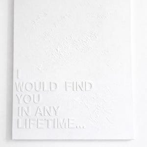 May include: A rectangular white canvas featuring a textured surface with the embossed white text I WOULD FIND YOU IN ANY LIFETIME... The artwork is monochromatic, utilizing raised lettering to create depth and shadow against the canvas background.