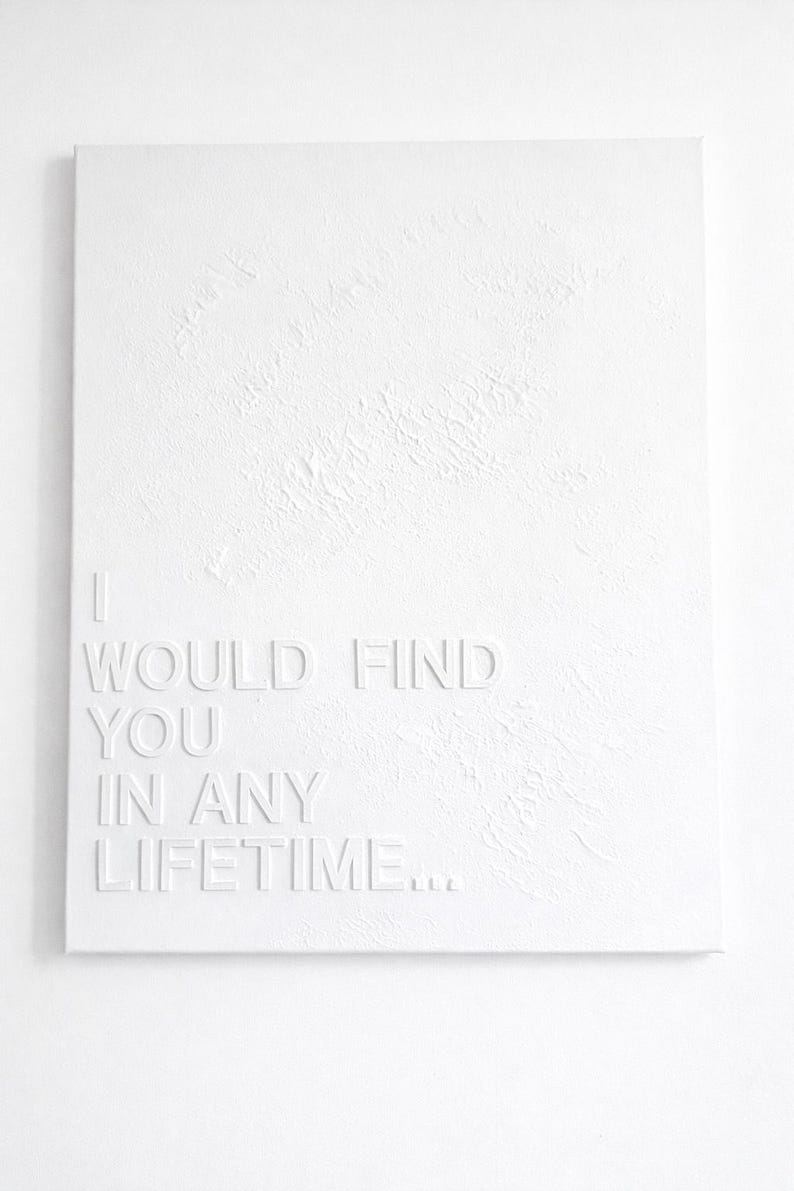 May include: A rectangular white canvas featuring a textured surface with the embossed white text I WOULD FIND YOU IN ANY LIFETIME... The artwork is monochromatic, utilizing raised lettering to create depth and shadow against the canvas background.