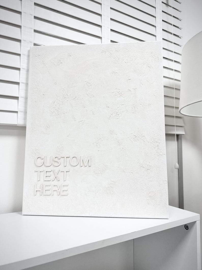 May include: A rectangular white canvas with a heavily textured, raised surface. The lower left corner features the embossed white text "CUSTOM TEXT HERE" in a clean, sans-serif font. The entire piece is monochromatic, showcasing a matte finish.