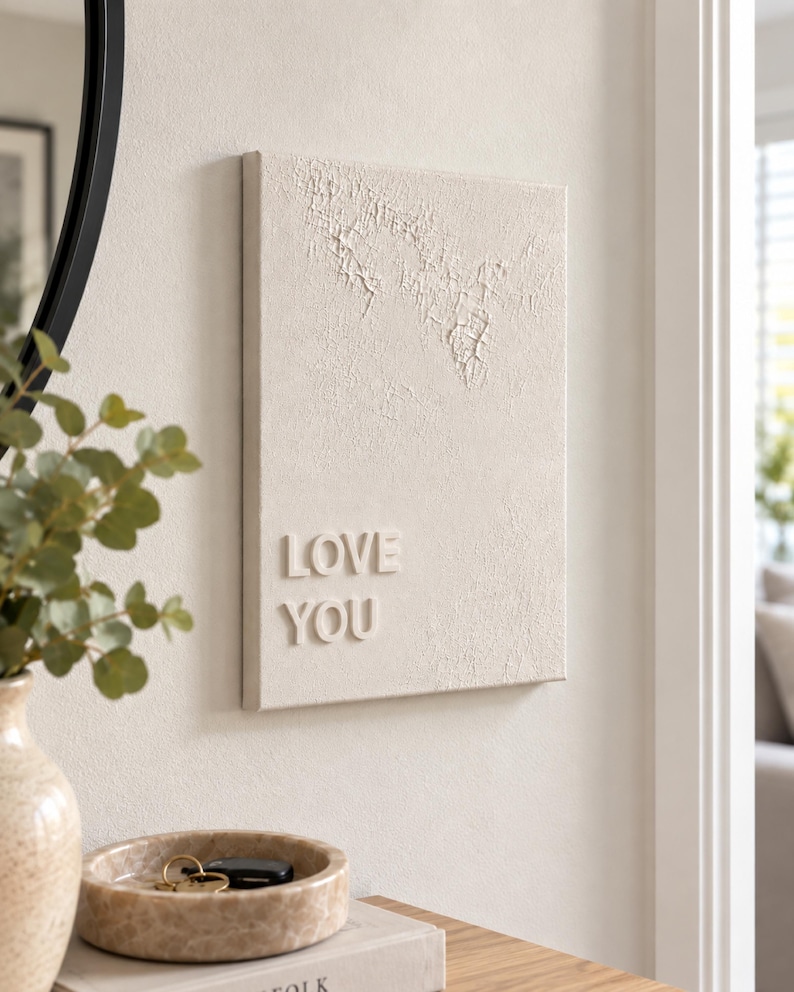 May include: A rectangular wall art piece in a neutral beige tone featuring a textured, cracked surface finish on the upper portion and the raised, three-dimensional lettering "LOVE YOU" in a clean, sans-serif font on the lower left side.