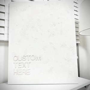 May include: A rectangular white canvas featuring a heavily textured, impasto-style surface. The lower left corner displays the embossed white text "CUSTOM TEXT HERE" in a clean, sans-serif font, creating a monochromatic and dimensional appearance.