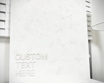 May include: A rectangular white canvas featuring a heavily textured, impasto-style surface. The lower left corner displays the embossed white text "CUSTOM TEXT HERE" in a clean, sans-serif font, creating a monochromatic and dimensional appearance.