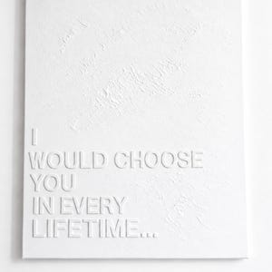 May include: A rectangular white canvas featuring a textured surface with raised white lettering that reads: I WOULD CHOOSE YOU IN EVERY LIFETIME... The artwork is monochromatic, with the text standing out against the subtle, uneven relief of the background.