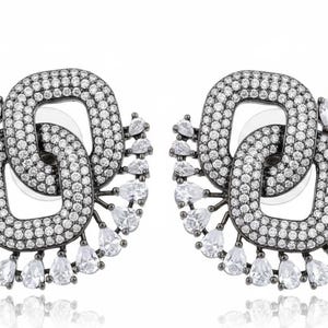 Peut inclure: Paire de boucles d'oreilles à clous argentées. Chaque boucle d'oreille présente deux maillons carrés imbriqués incrustés de petits cristaux ronds et transparents. Des cristaux en forme de goutte d'eau pendent du bas de chaque boucle d'oreille.