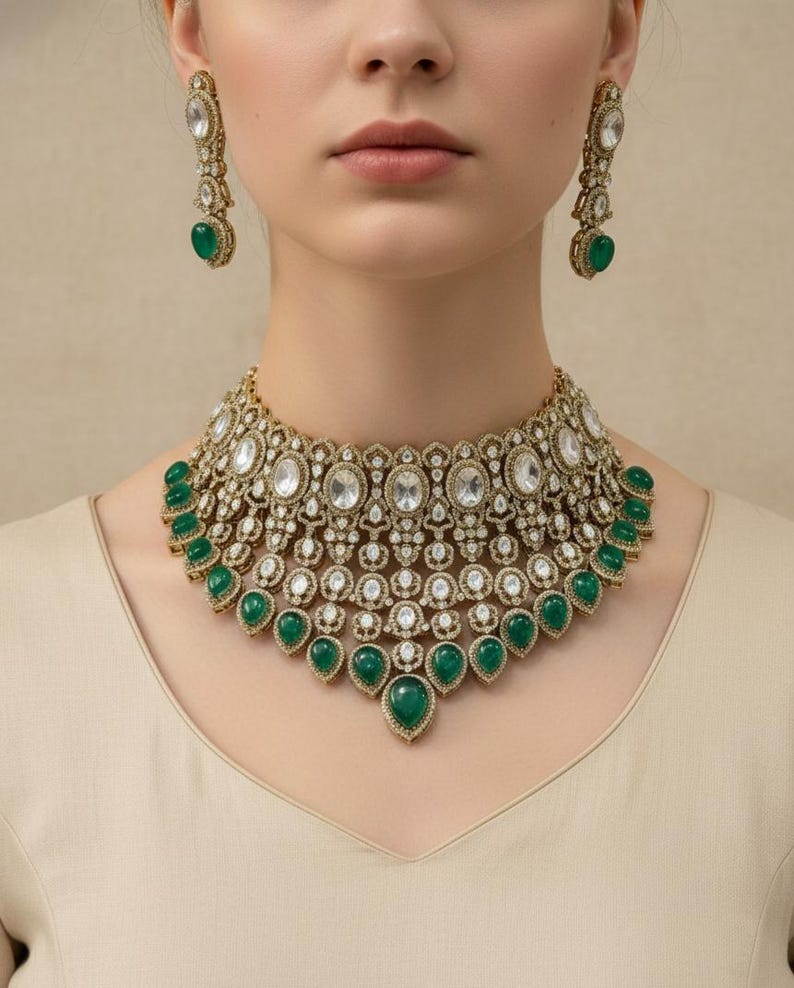 Op de afbeelding: Een goudkleurige ketting en bijpassende oorbellen set. De ketting heeft heldere, ovaal geslepen stenen en druppelvormige smaragdgroene stenen. De oorbellen hebben een vergelijkbaar ontwerp met een grote smaragdgroene steen.
