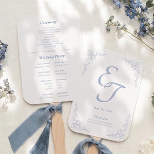 Könnte beinhalten: Zwei fächerförmige Hochzeitsprogramme mit abgerundeten Ecken, gedruckt auf weißem Karton mit blauem Text. Eine Seite listet die Zeremonie und die Hochzeitsgesellschaft auf, die andere zeigt die Initialen E und J, das Datum 17. Mai 2026 und eine blaue Quaste.