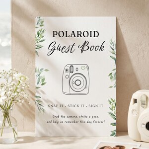 May include: A white rectangular guest book sign featuring green leaf illustrations, a line drawing of a camera, and the text: POLAROID Guest Book, SNAP IT · STICK IT · SIGN IT, Grab the camera, strike a pose, and help us remember this day forever!
