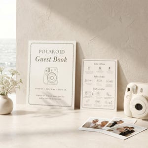 May include: A cream-colored Polaroid guest book sign with a line drawing of a camera, a matching instruction card with icons, and a white instant camera. Three small square instant photos are displayed on the surface in front of the items.