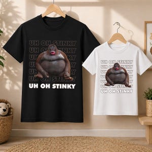 May include: Black and white t-shirts with a graphic of a gorilla and the text "UH OH STINKY". The gorilla is brown with a red mouth. The shirts are hanging on wooden hangers.
