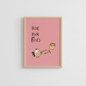 Könnte beinhalten: Gerahmter Kunstdruck mit rosa Hintergrund. Er zeigt eine Cartoon-Vogel-Figur, die zwei Pommes Frites hält, mit einer kleinen Krone. Der Text "HIDE YOUR FRIES" steht über dem Vogel und den Pommes Frites.