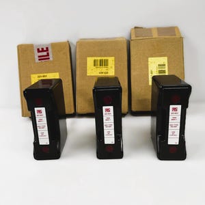 Op de afbeelding: Drie zwarte elektrische zekeringen met rode accenten en witte labels, voor drie kartonnen dozen. De zekeringen hebben het RS-logo en technische specificaties. De dozen hebben labels en barcodes.