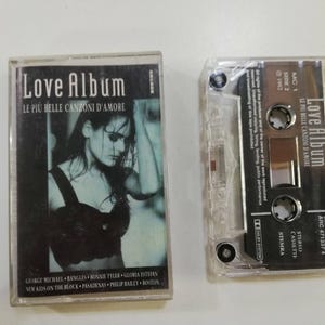 Può includere: Una musicassetta Love Album con custodia in plastica trasparente e copertina in bianco e nero che ritrae una persona con un top scuro. La cassetta è trasparente con un'etichetta nera che riporta il testo Love Album, 1992 e altri dettagli.