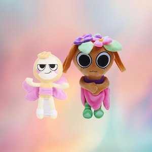 Peut inclure: Deux poupées en peluche. L'une est une fée jaune clair et rose avec un visage souriant et des ailes de papillon. L'autre est une poupée marron avec de grands yeux noirs, une couronne de fleurs et une robe rose. Les poupées sont sur un fond dégradé.