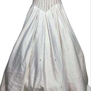 May include: A white wedding gown with a beaded bodice and a full skirt. The bodice features vertical rows of beads, and the skirt has a flowing, layered design. Small, scattered embellishments add detail to the skirt.