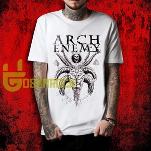 May include: White t-shirt featuring the band name "ARCH ENEMY" above a detailed black and white illustration of a horned goat-like figure with multiple eyes and a skull. The shirt is a classic crew neck.