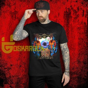 Peut inclure: T-shirt noir avec un motif graphique coloré affichant le nom du groupe "Mastodon" et le texte "Crack the Skye". Le motif comprend deux personnages et un élément circulaire central. Une casquette de baseball noire avec le logo du groupe est également visible.