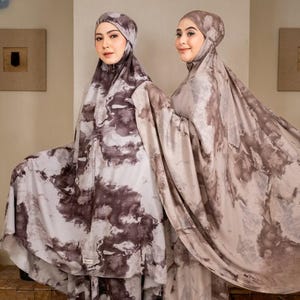 May include: Two women wearing matching prayer garments. The garments are a light colour with a dark brown, marbled pattern. Each woman is also wearing a matching head covering. The background is a neutral colour.