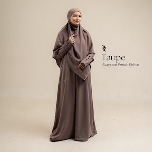 May include: A taupe abaya set with a French khimar, featuring a long, flowing dress and a matching head covering. The sleeves have button details at the cuffs. The text on the right reads Taupe Abaya set French Khimar.