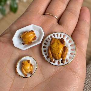 Può includere: Tre polli arrosto in miniatura serviti su piccoli piatti bianchi. Un pollo è posto su un piatto bianco esagonale, un altro su un piccolo piatto rotondo con bordo dorato e il più grande su un piatto rotondo con bordo traforato dorato.