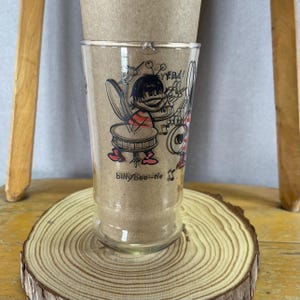 Peut inclure: Un verre transparent avec une illustration de dessin animé d'une abeille jouant des instruments de musique. L'abeille porte une chemise à rayures rouges et blanches. Le verre porte l'inscription "billy bee-tle" et des notes de musique.