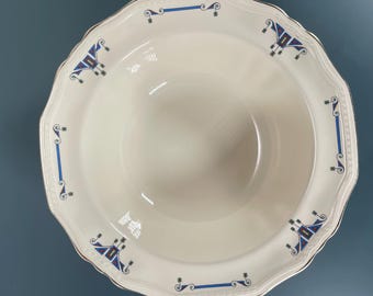 May include: A cream-colored ceramic bowl with a scalloped edge and a silver-toned rim. The wide rim features a repeating geometric pattern in blue, red, and black, consisting of linear bars and stylized angular motifs spaced evenly around.