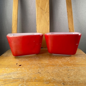 Op de afbeelding: Twee rechthoekige glazen kommen met een felrode buitenkant en een gladde witte binnenkant. Deze bakjes hebben afgeronde hoeken en een taps toelopende vorm, met een stevige bodem en een open bovenkant, wat een strak ontwerp laat zien.
