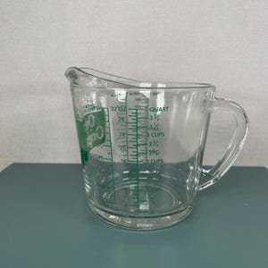May include: Clear glass measuring cup with a handle and a pouring spout. Green markings indicate measurements in cups, ounces, and quarts. The cup has a capacity of 4 cups or 32 ounces.