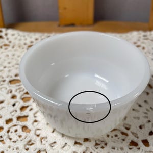 May include: A white, round bowl with a slightly textured exterior. The bowl has a smooth, glossy interior and a thick rim. The bowl is likely made of ceramic or glass and is suitable for serving food or as a decorative item.