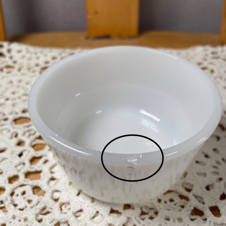 May include: A white, round bowl with a slightly textured exterior. The bowl has a smooth, glossy interior and a thick rim. The bowl is likely made of ceramic or glass and is suitable for serving food or as a decorative item.