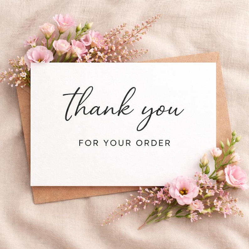 May include: A white card with the words "Thank you FOR YOUR ORDER" in black script is placed on a brown envelope. Pink flowers and greenery surround the card, set against a neutral fabric background.