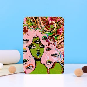 May include: A rectangular art print featuring a surreal illustration of a woman with multiple eyes and pink hair. The woman's face is green with blue lips. The background has a paisley design with pink, green, and gold colors.