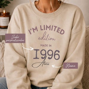 May include: A beige crewneck sweatshirt featuring the dark purple text I'M LIMITED edition MADE IN 1996 and the name Alice in a cursive script. The design includes arrows pointing to the year and name with labels Jahr personalisierbar and Name.