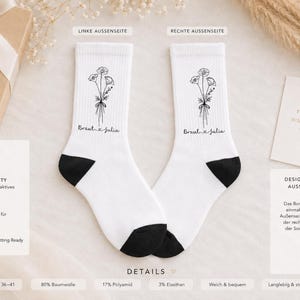 Pode incluir: Um par de meias brancas com calcanhar e ponta pretos, apresentando uma ilustração de ramo de flores em linha preta e o texto Braut & Julia impresso no lado exterior, feitas de 80% algodão, 17% poliamida e 3% elastano.